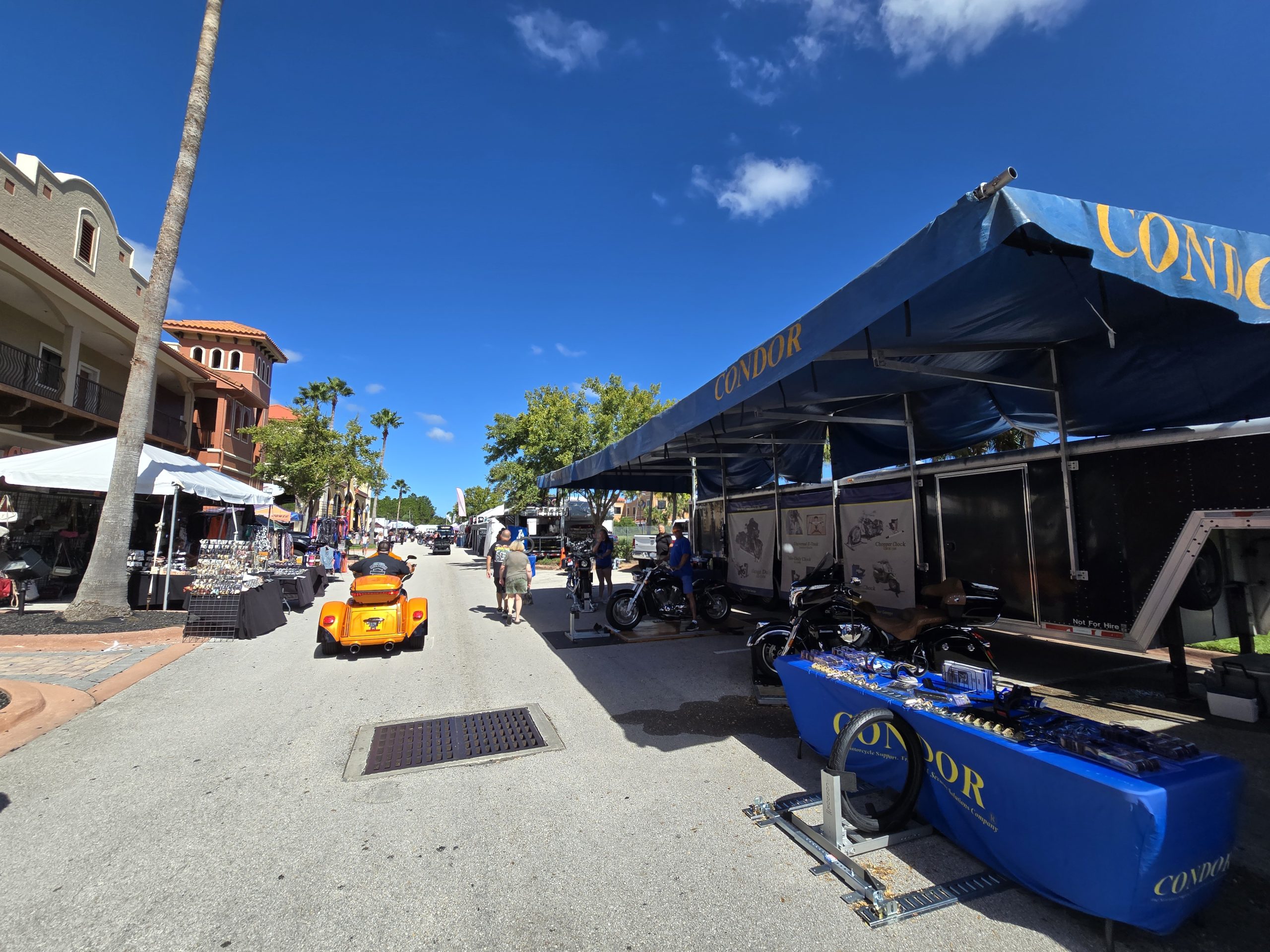 Street fair with stalls and motorcycles under blue sky.
