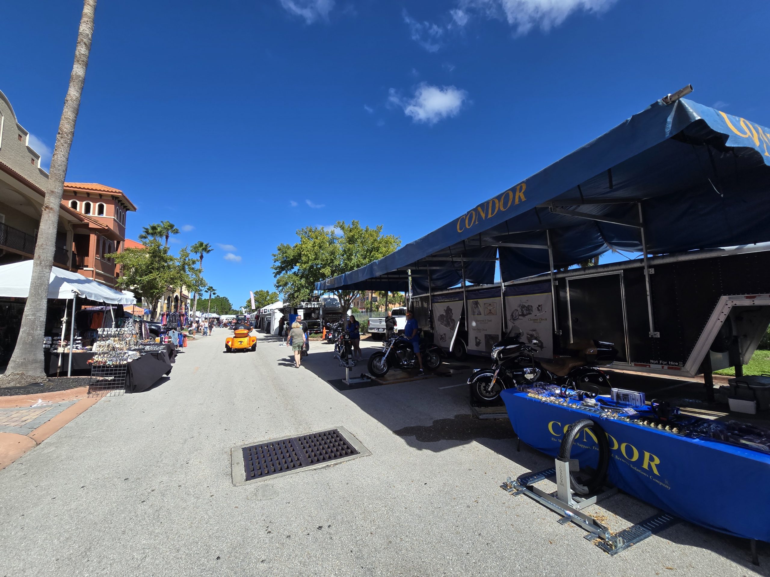 Outdoor market with motorcycles and vendors under blue sky.